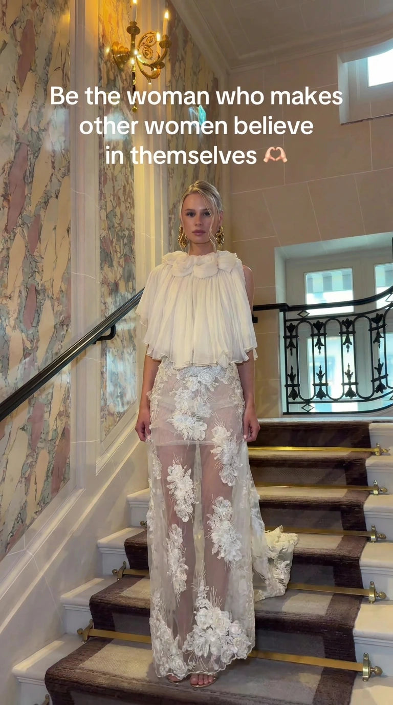 Front full view of Ivory pleated capelet floral embroidered maxi gown on staircase