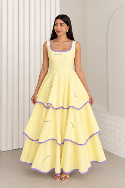 Model wearing pastel yellow sleeveless tiered maxi dress with purple contrast trim, front view