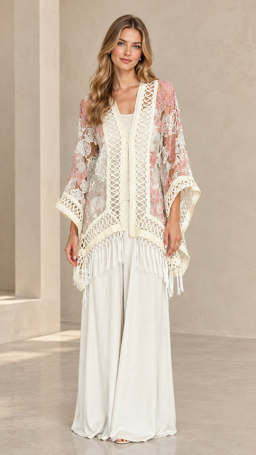 Front view of woman wearing blush pink floral lace fringe kimono with white wide-leg pants