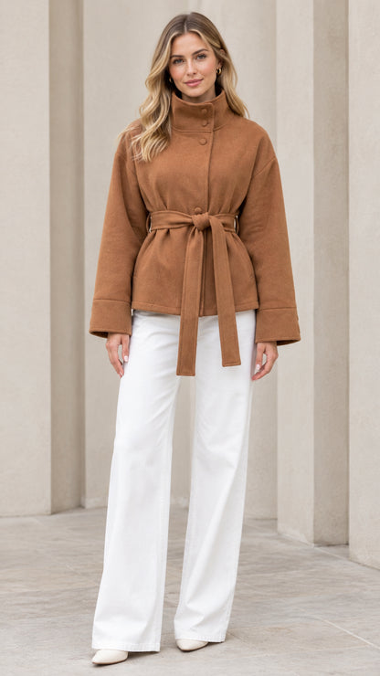 Front view of model wearing camel stand collar belted short coat with white trousers