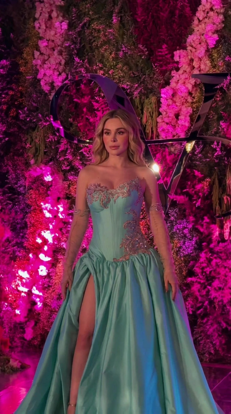 Front view of woman wearing turquoise strapless corset evening gown with high slit and embroidery