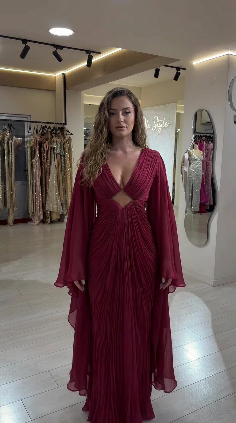 Front view of model wearing burgundy pleated maxi evening gown with cape sleeves and front cutout