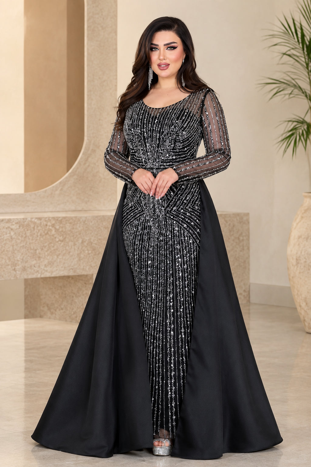 Front view of black embellished long-sleeve evening gown with sweeping overskirt