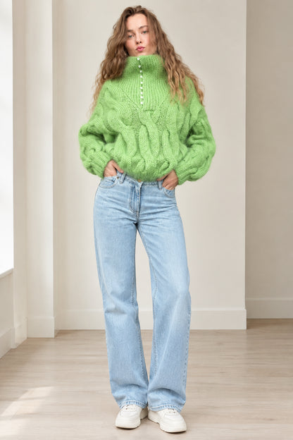 Front full-length view of model wearing lime green chunky cable knit high neck sweater with light wash jeans