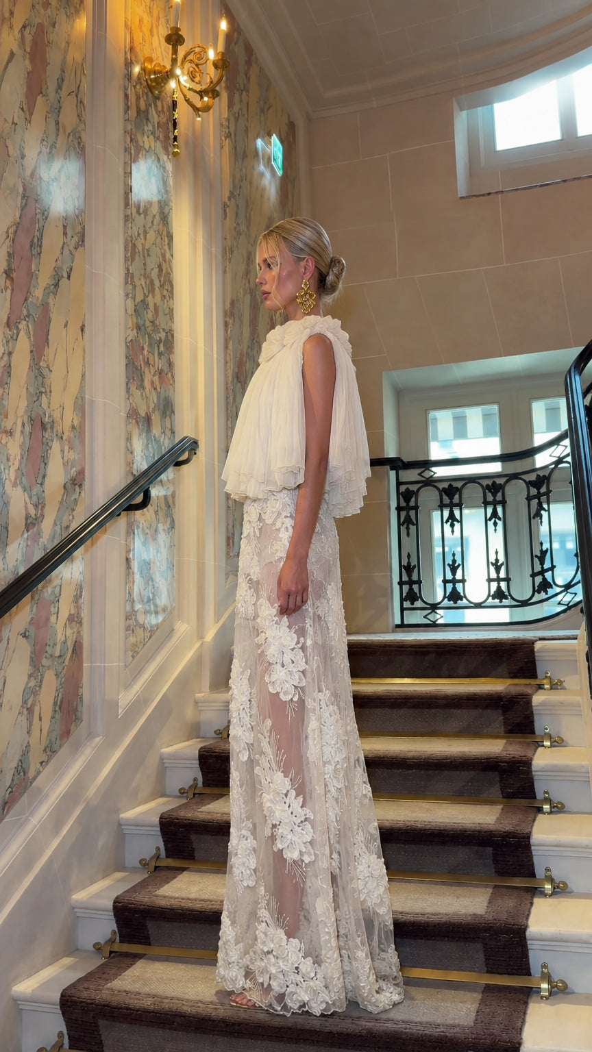 Side profile view of woman wearing Ivory floral lace gown with pleated capelet overlay