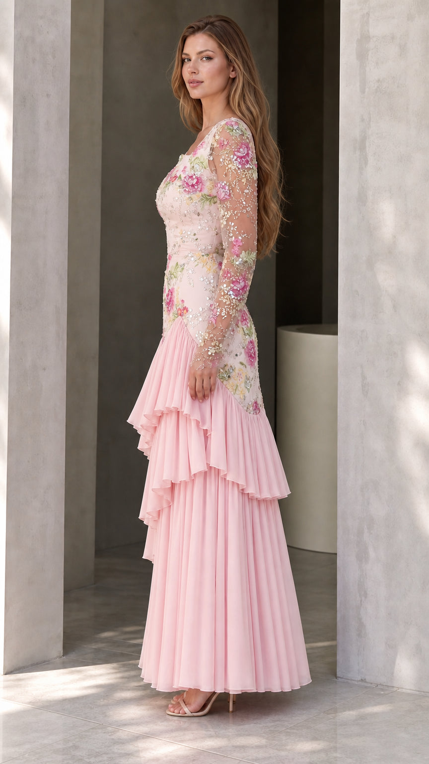 Side angle view of woman modeling pink long sleeve embroidered gown with pleated tiered hem