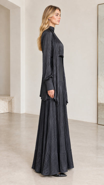 Side profile view of black mock-neck pleated maxi dress and matching long cardigan