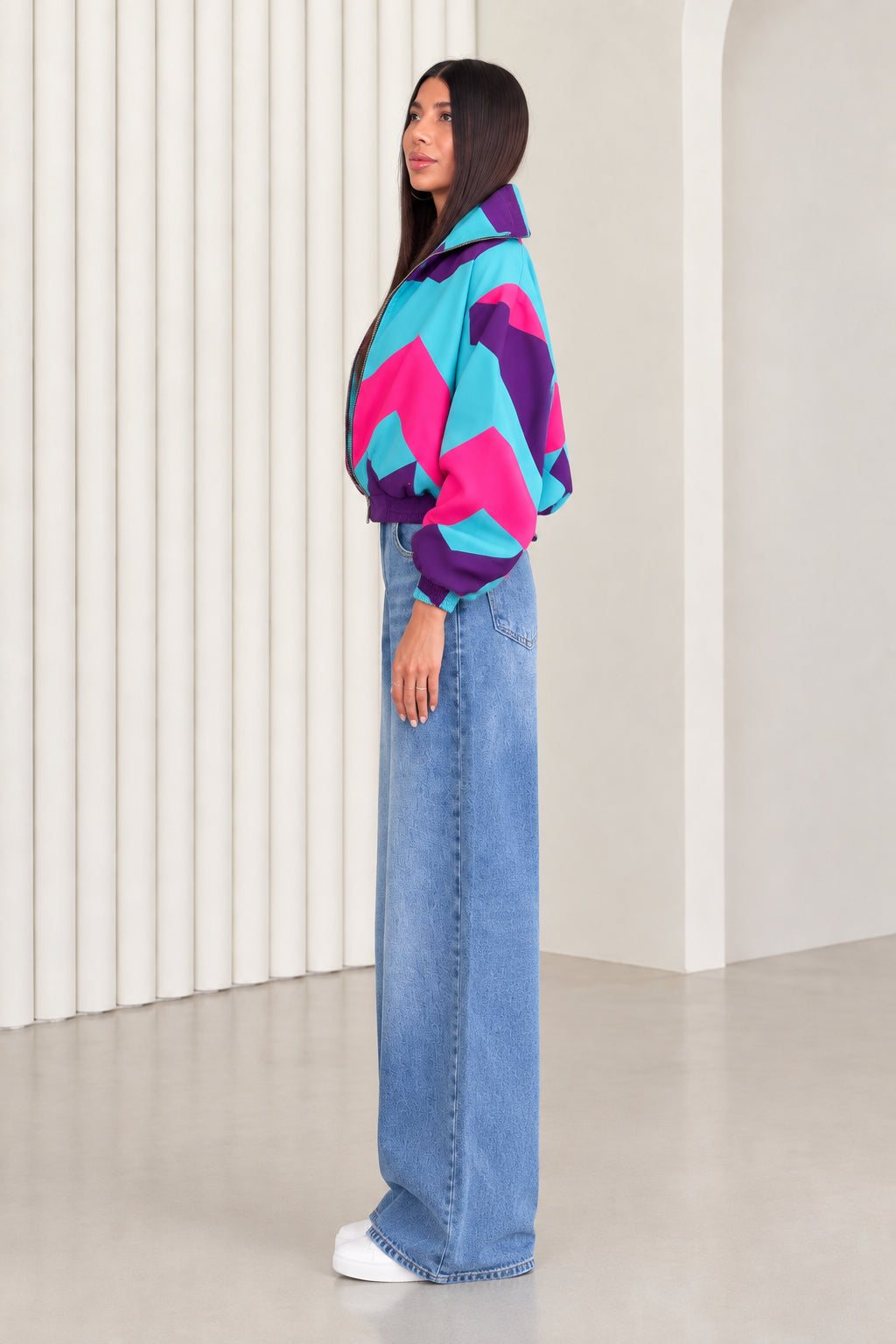 Side profile view of woman wearing purple and turquoise colorblock cropped windbreaker jacket