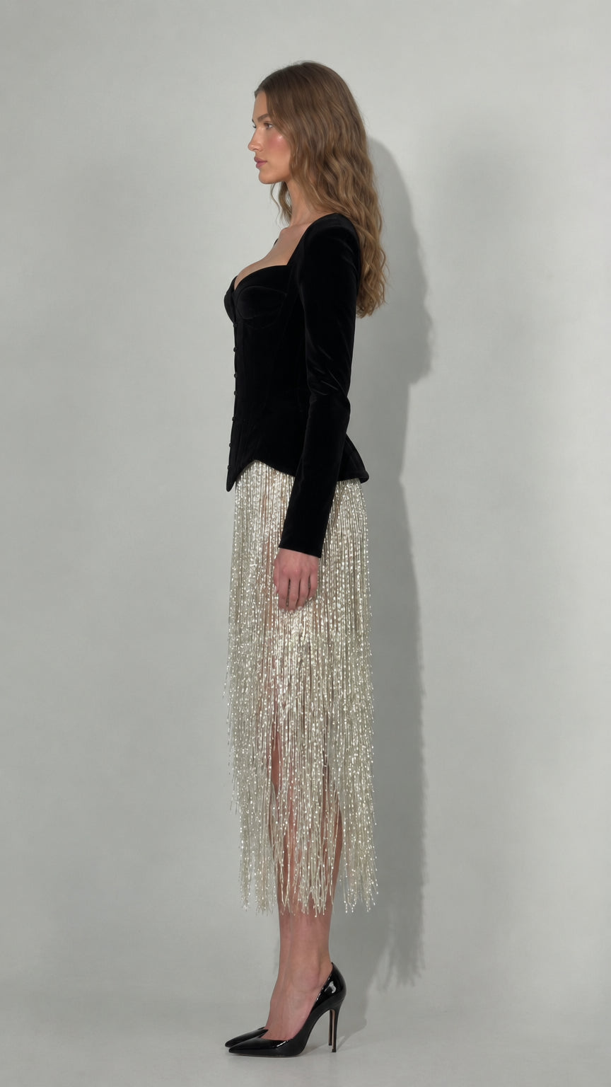 Side profile of black velvet corset midi dress with flowing fringe skirt