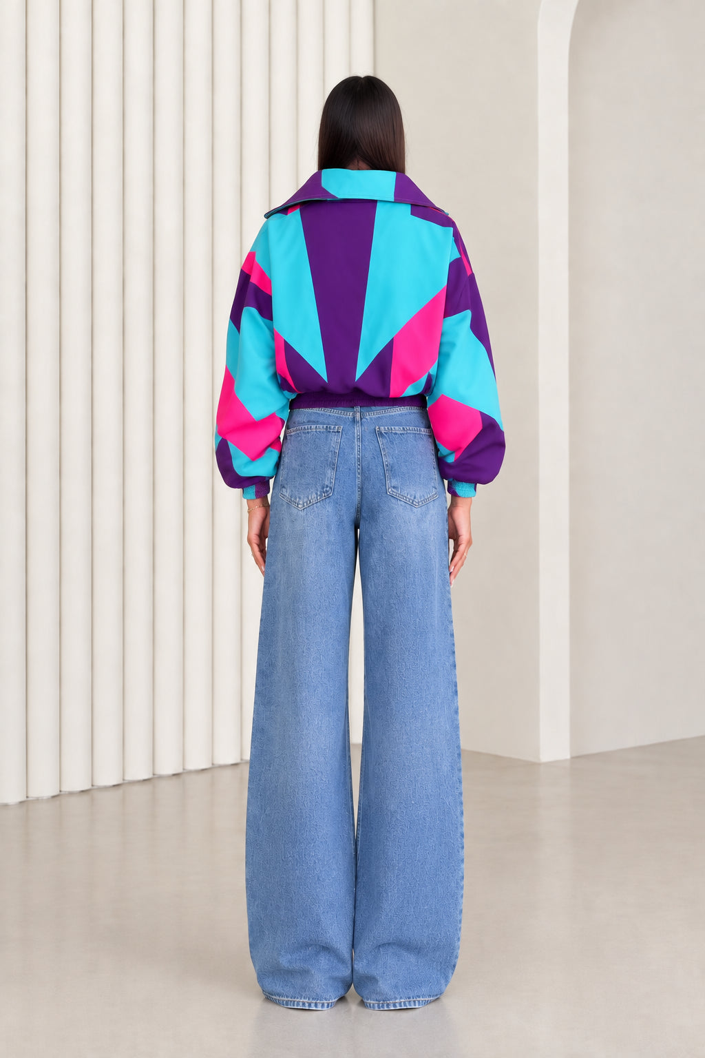 Back view of woman showing geometric starburst colorblocking on purple and turquoise windbreaker jacket