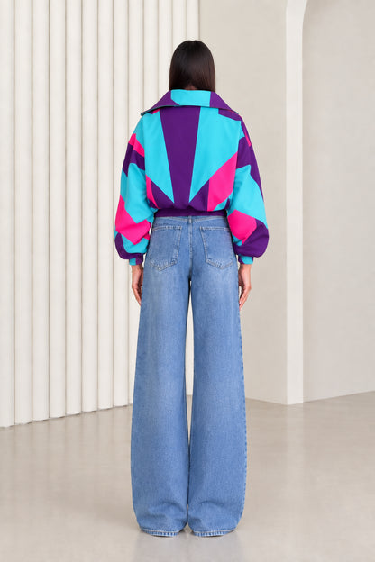 Back view of woman showing geometric starburst colorblocking on purple and turquoise windbreaker jacket