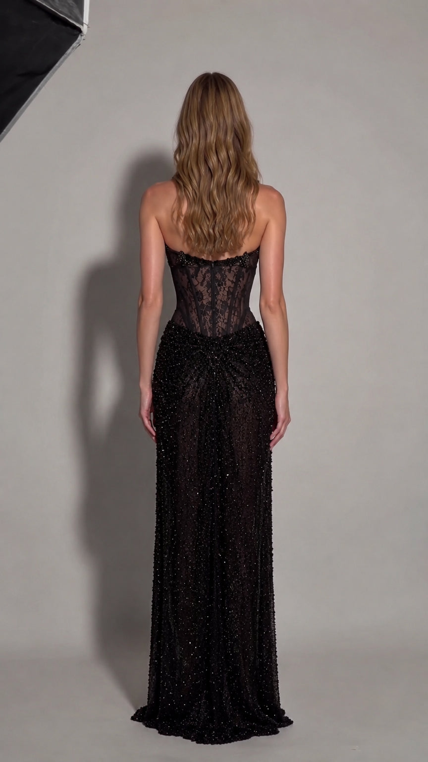 Back view of model showing open back and beaded maxi skirt of black formal gown