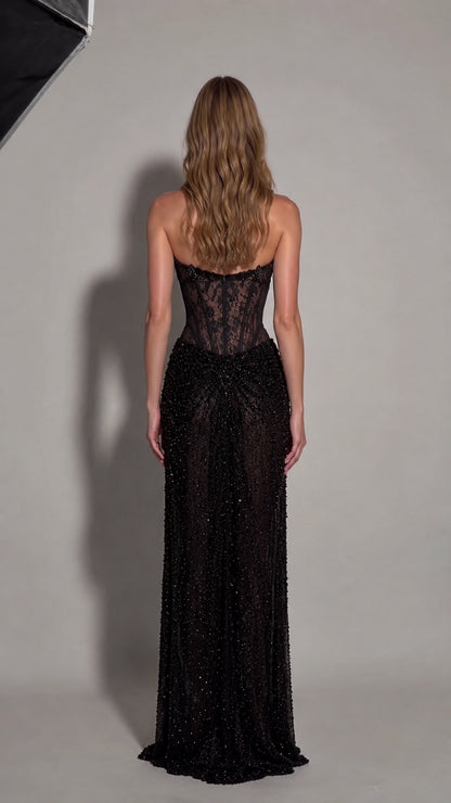 Back view of model showing open back and beaded maxi skirt of black formal gown