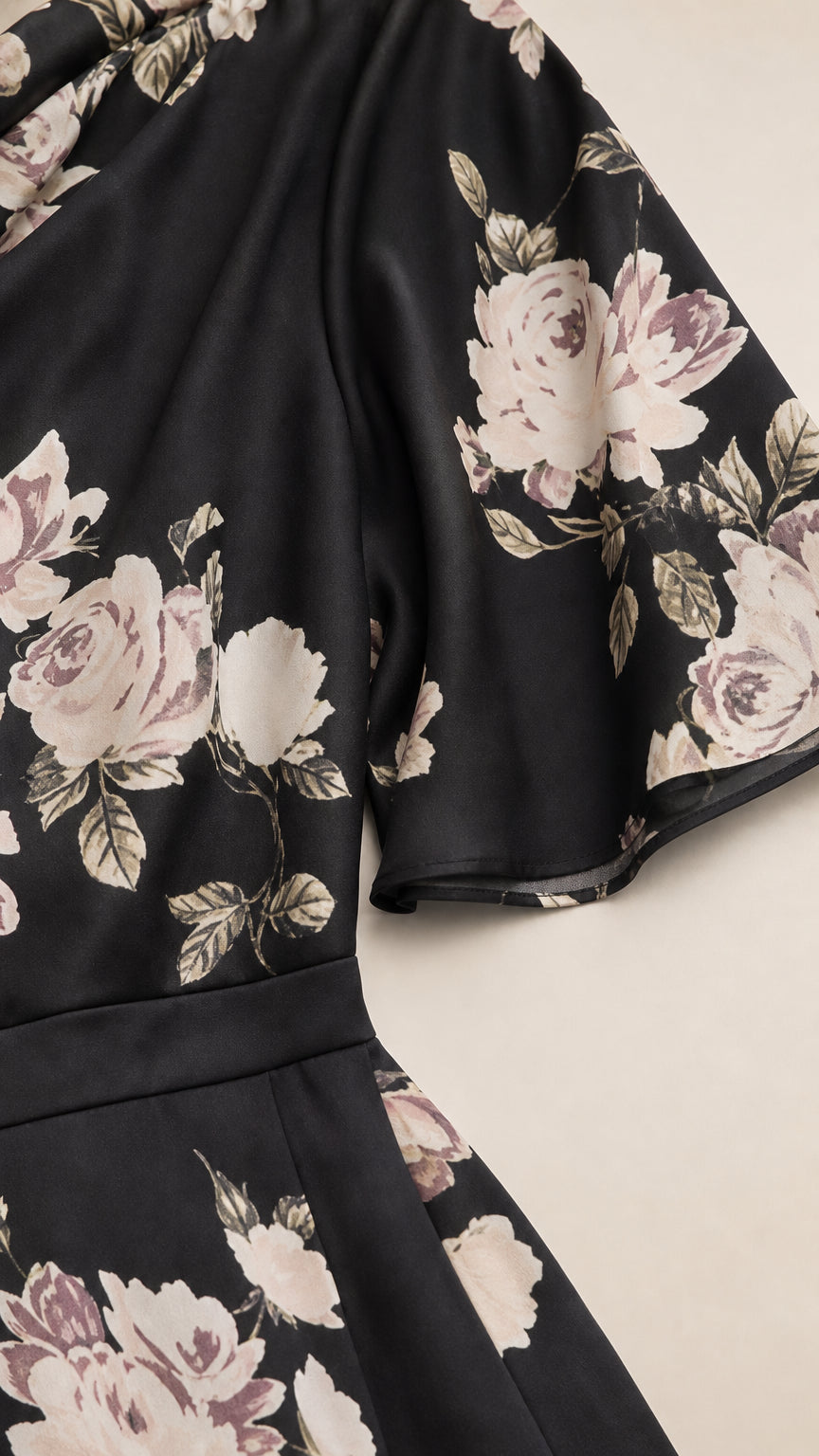 Close-up detail of black floral fabric, draped shoulder, and flutter sleeve