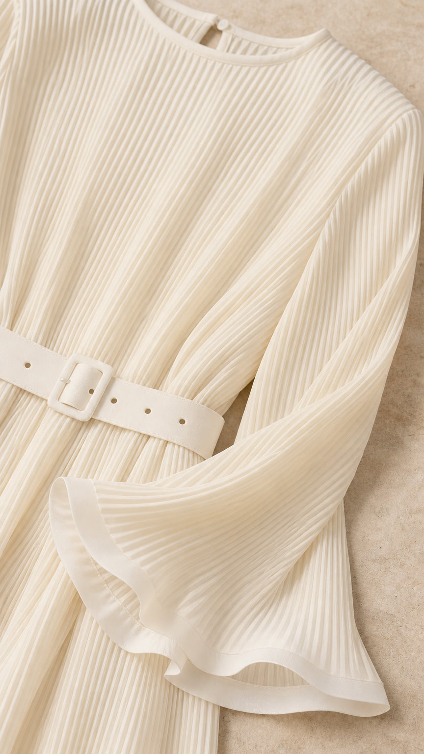 Close-up detail of cream accordion pleated fabric, matching belt buckle, and flared cuff