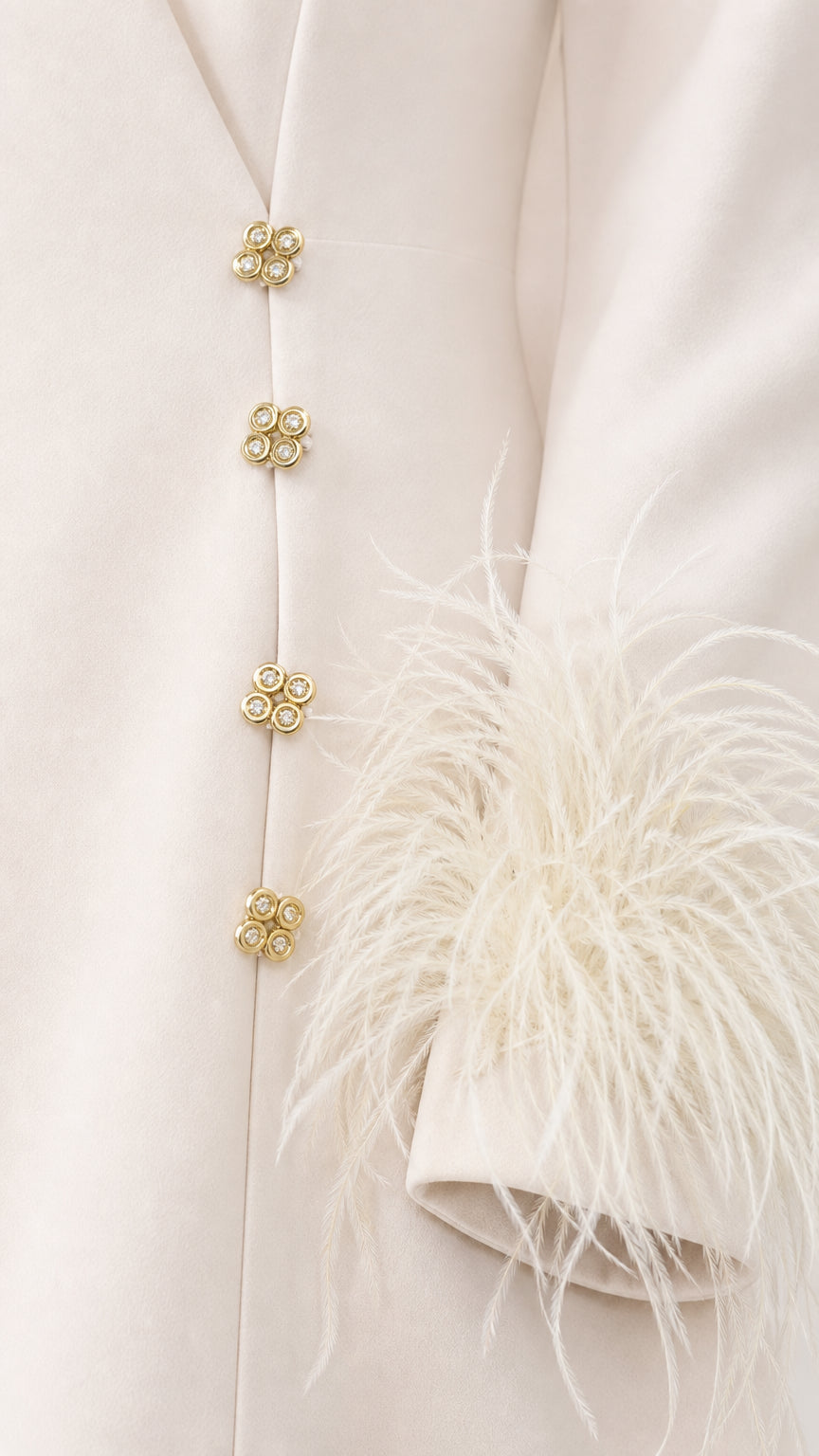 Close-up detail of ornate gold-tone buttons and wispy feather cuff trim on ivory fabric