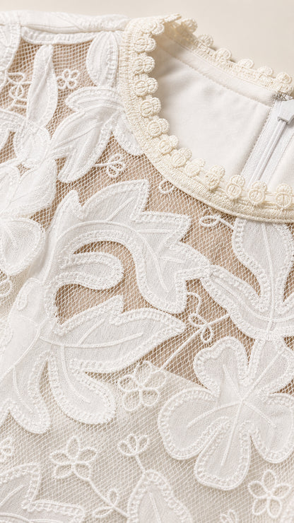 Close-up detail of white floral embroidery and beaded pearl-like trim along the neckline