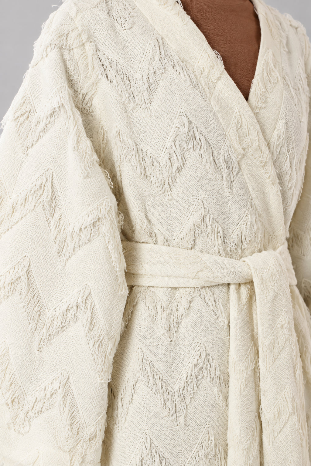 Close-up detail of cream textured chevron fabric and fringe trim with tie belt