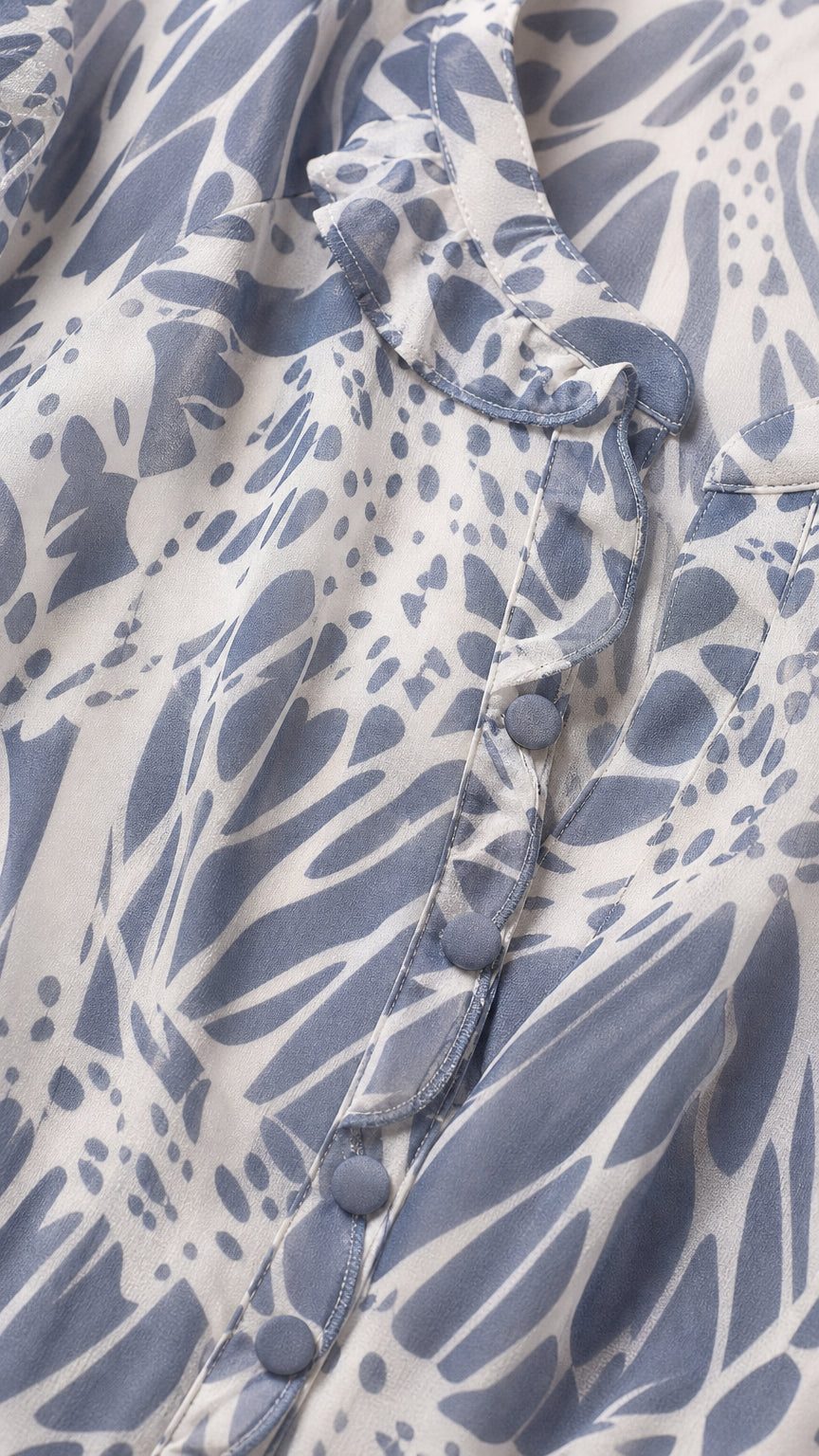 Close-up detail of dusty blue floral fabric, ruffled neckline, and covered buttons