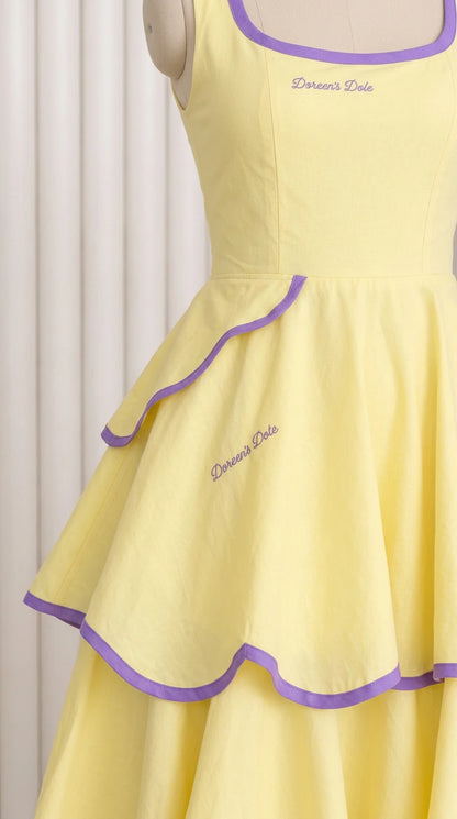 Close-up detail of square neckline and tiered ruffles with purple trim on pastel yellow dress