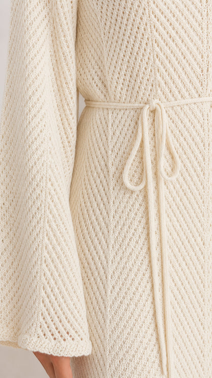 Close-up detail of textured chevron knit fabric, tie belt, and bell sleeve hem