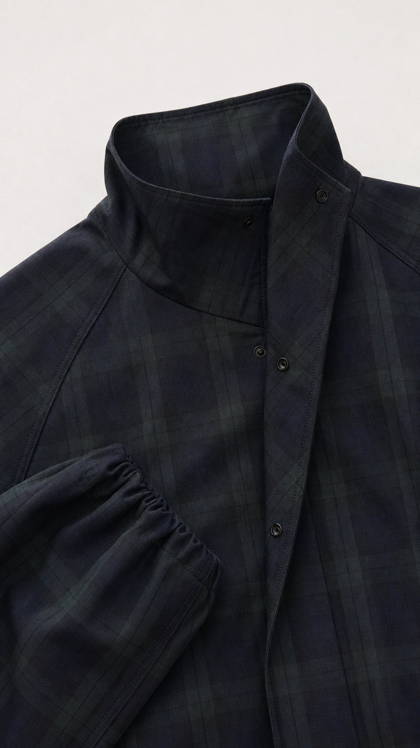 Close-up detail of the snap-button high stand collar and sleeve cuff on dark plaid jacket
