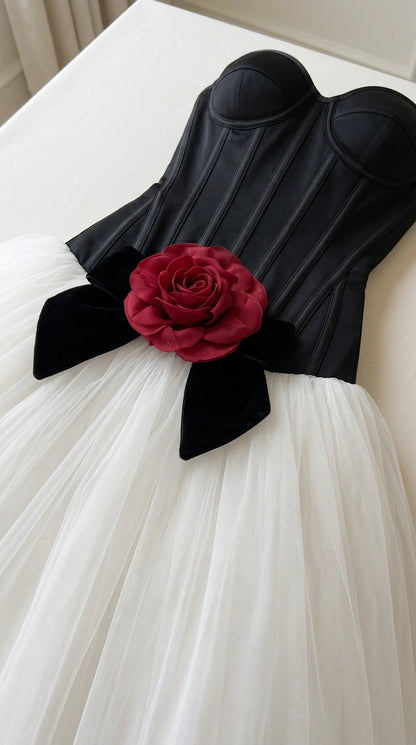Close-up detail of black corset bodice, red rose appliqué, black bow, and white tulle skirt