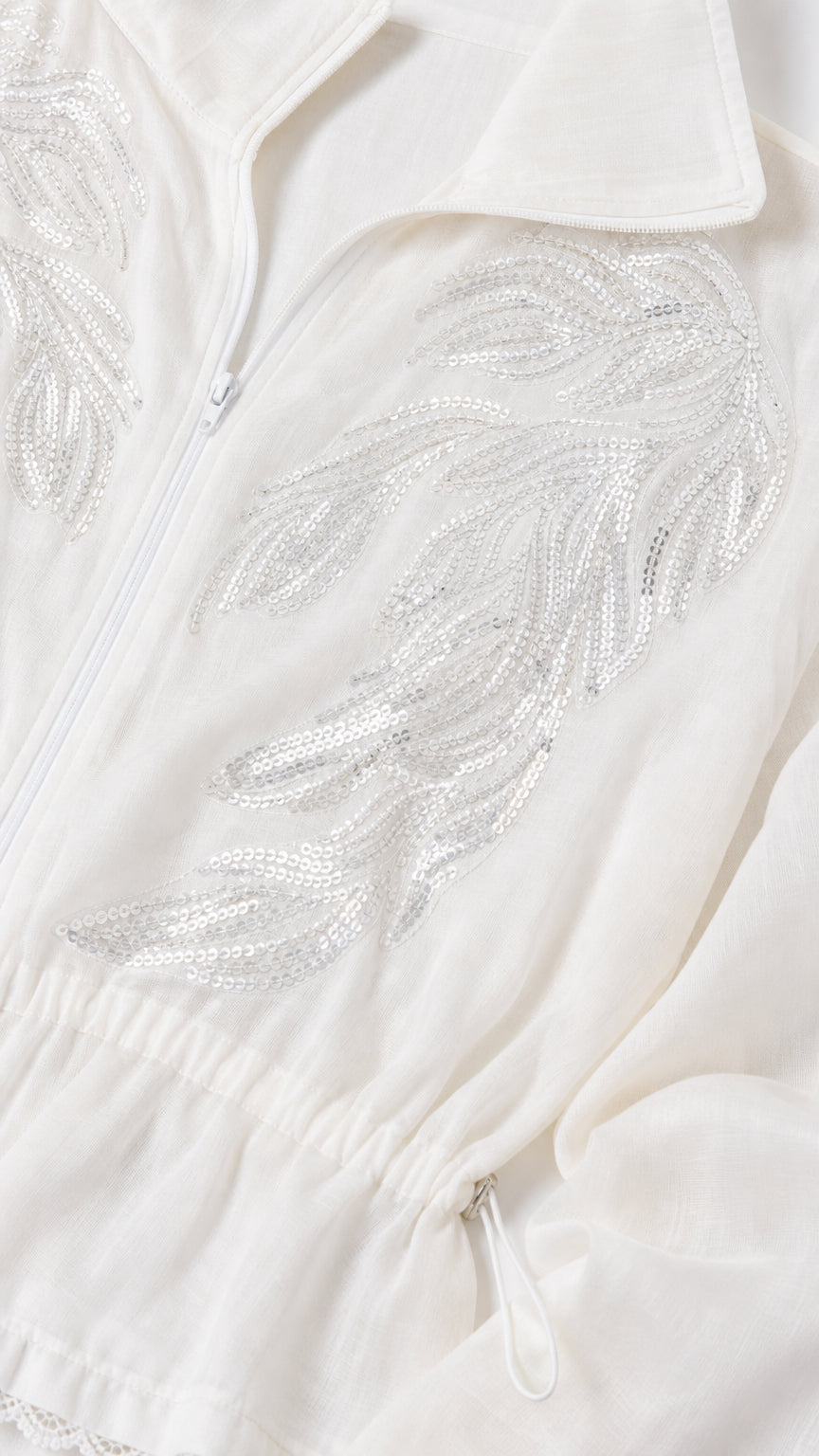 Close-up of intricate silver sequin leaf embroidery on white zip-up jacket