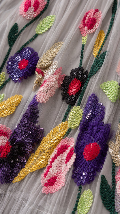 Close-up detail of colorful floral embroidery and sparkling sequins on fine grey tulle