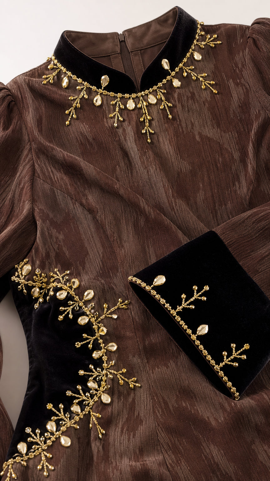 Close-up detail of neckline and cuff embroidery on textured brown fabric