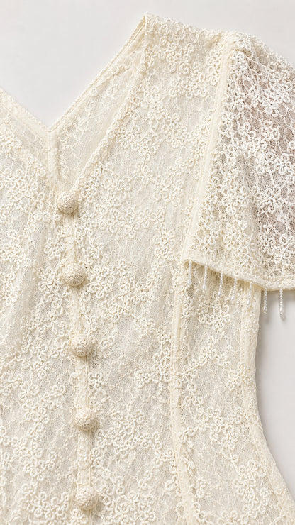 Close-up of cream floral lace fabric, V-neckline, and covered button front details