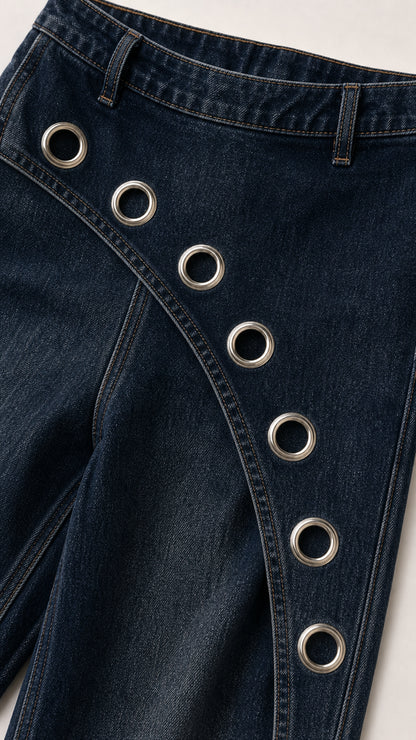 Close-up detail of dark blue denim fabric and metal grommet trim across waist and leg