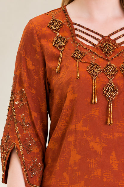 Close-up detail of caged strappy V-neckline with intricate beaded motifs on rust dress