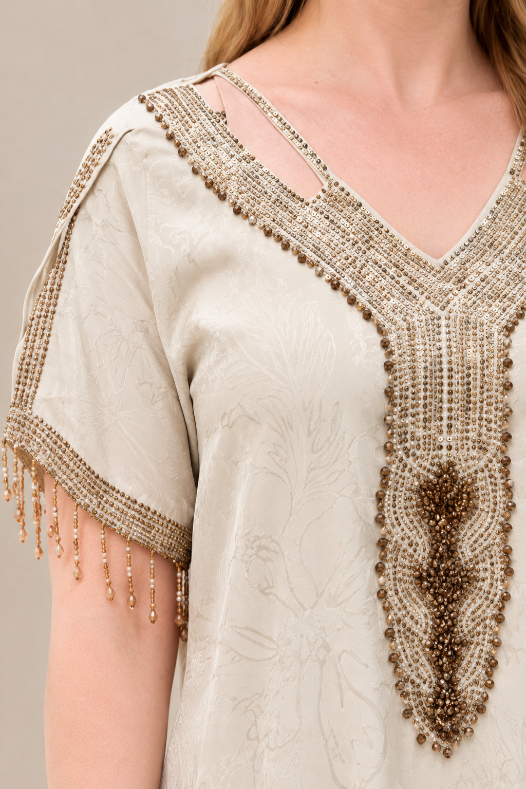Close-up of beaded V-neckline, strap detail, and fringed sleeve trim