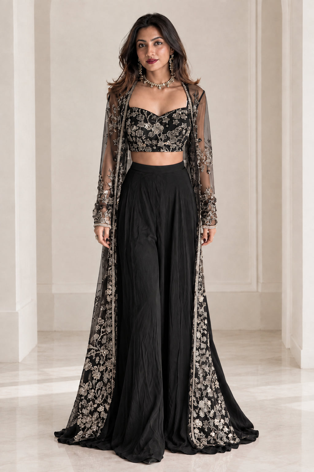 Model wearing black embroidered sweetheart crop top and wide-leg palazzo set with sheer cape