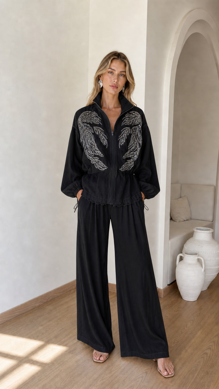 Front full view of woman wearing black embroidered zip jacket and wide-leg pants set