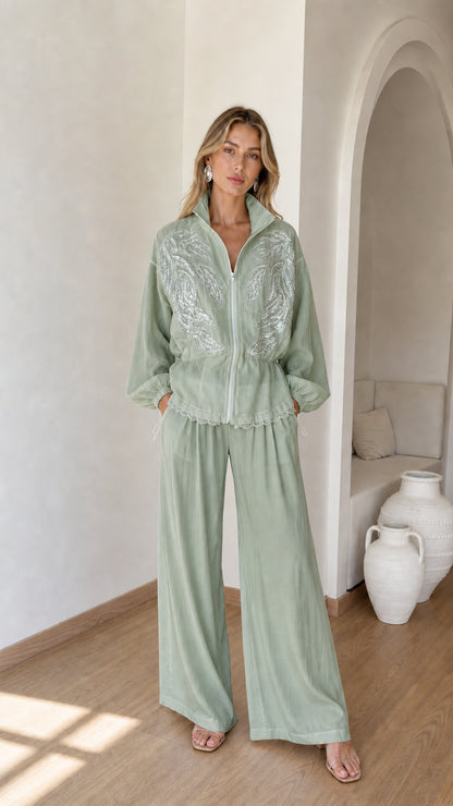 Front full view of woman wearing sage green embroidered zip jacket and wide-leg pants set