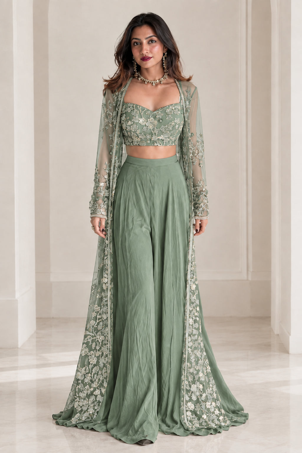 Model wearing sage green embroidered crop top and wide-leg trousers with floor-length sheer cape