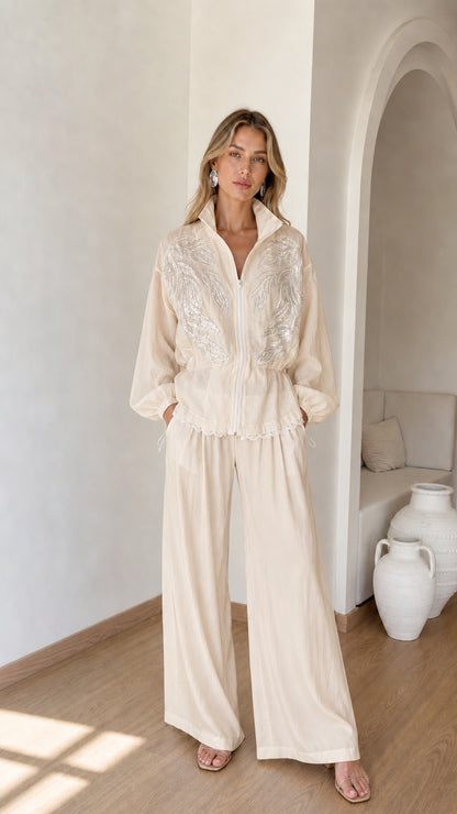 Front full view of woman wearing beige cream embroidered zip jacket and wide-leg pants set